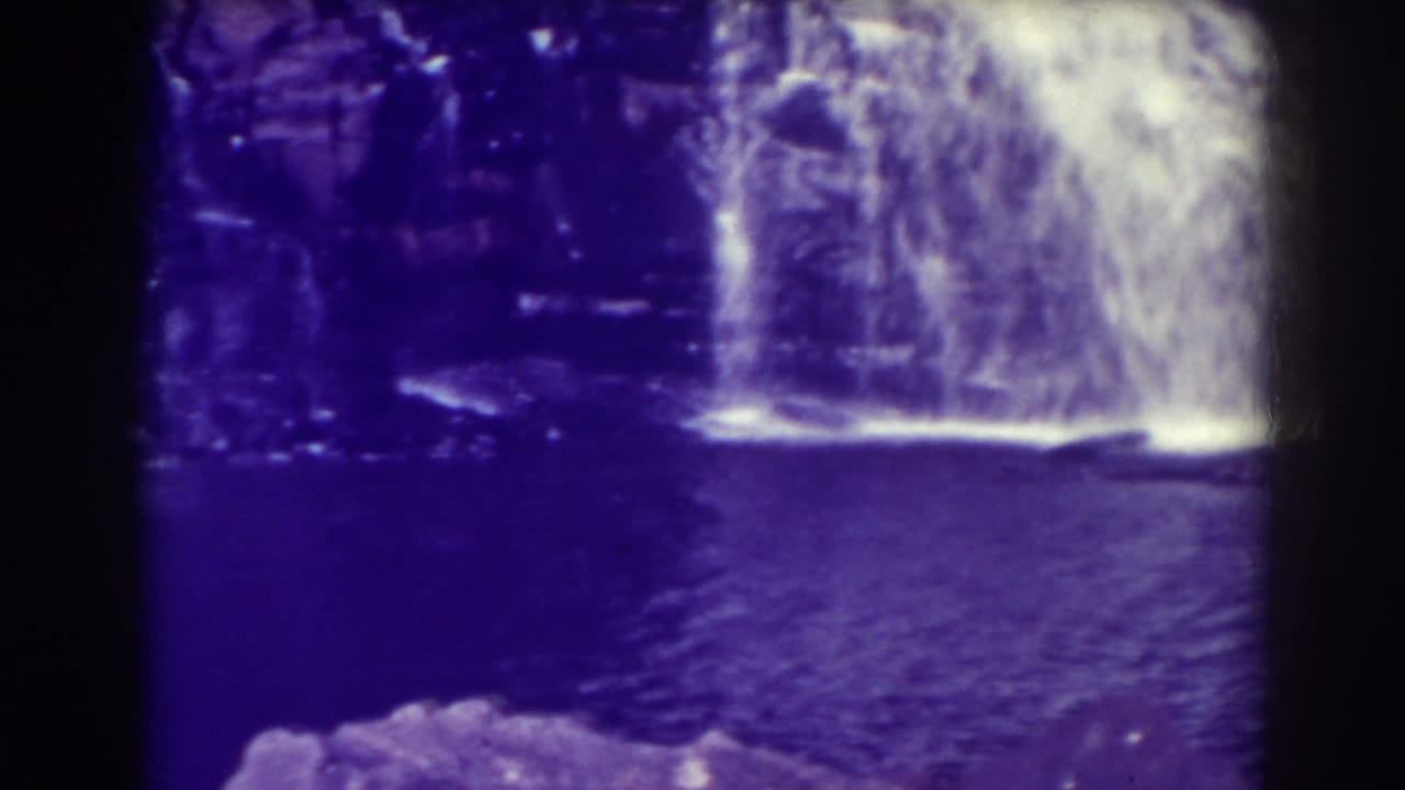Waterfall dropping over a rock ledge into a dark pool with heavy film borders.