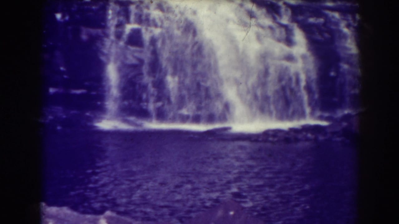 Blackwater Falls, West Virginia, seen in a 1938 8mm frame with a broad white cascade, dark pool, rocky cliff, and strong purple film cast.