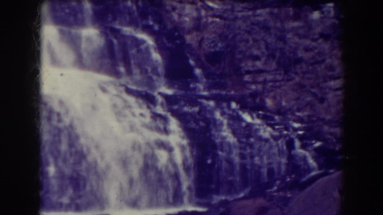 Water cascades over layered rock ledges with a dark vertical film divider at center.