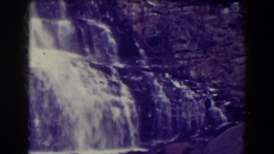 1938 8mm view of Blackwater Falls, West Virginia, with pale water spilling over rock ledges and a dark contact-sheet divider at center.
