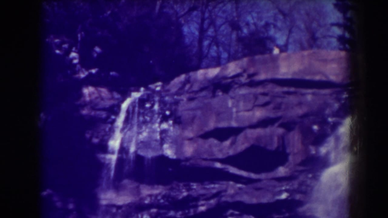 Waterfall dropping over layered rock with dark trees above and heavy edge vignetting.