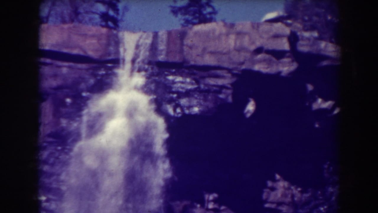 Waterfall spilling over dark rocks with treetops and film border visible.