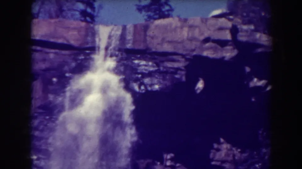 1938 Blackwater Falls home-movie frame showing white water dropping over dark rock ledges beneath a small strip of sky and trees.