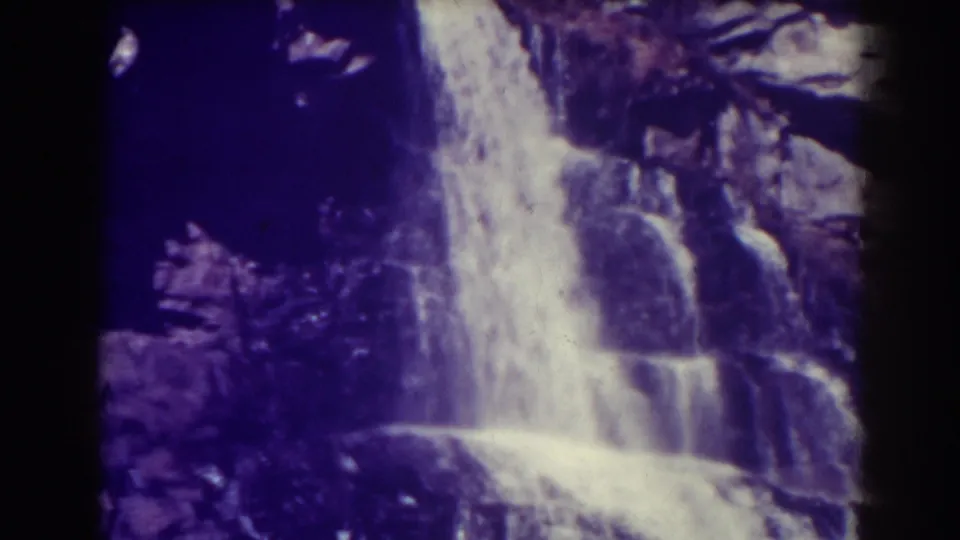 Late-1930s home-movie view of Blackwater Falls, showing water sliding down stepped rock shelves with heavy shadow and color shift.