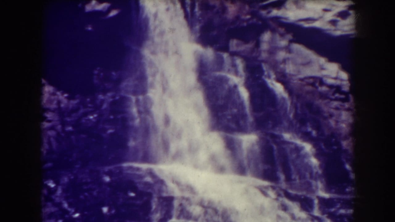 Waterfall dropping over dark layered rocks with black film borders visible.