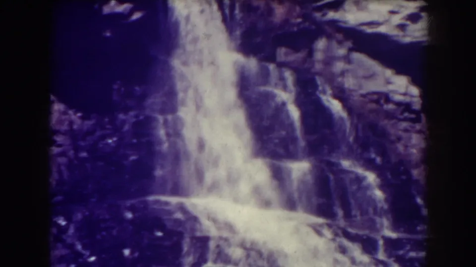 1938 8mm view of Blackwater Falls, with white water pouring over dark rock ledges and a strong purple film cast.