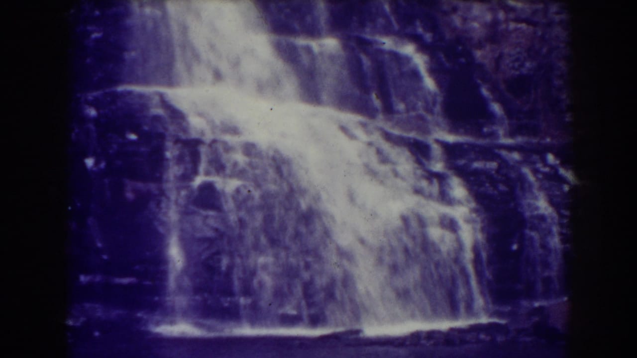 Water cascades over dark rock ledges into a shadowed pool.