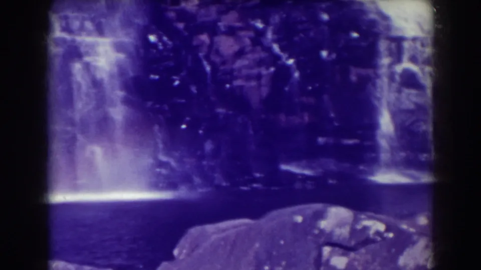 A purple-shifted 1938 home-movie frame shows Blackwater Falls flowing into a pool with dark rocks in front.