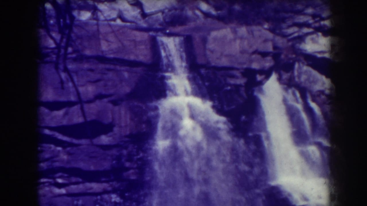 Waterfall spilling over dark rock ledges with bare branches above.