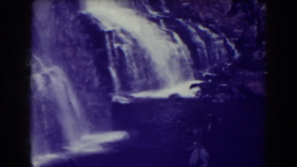 1938 8mm view of Blackwater Falls cascading over rocky ledges into dark water, with soft focus and purple-blue aging.