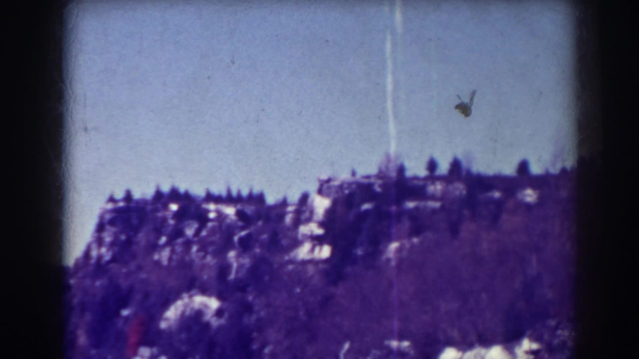 Distant rocky ridge and treetops beneath pale blue sky with a vertical film streak.