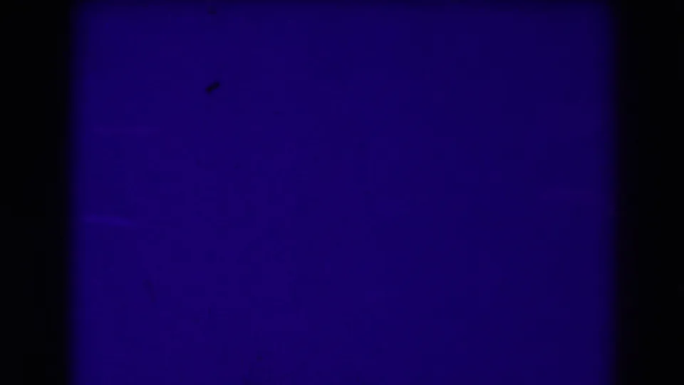 Blue end-of-reel or leader-like frame from the 8mm clip, with faint surface marks and dark bordering.