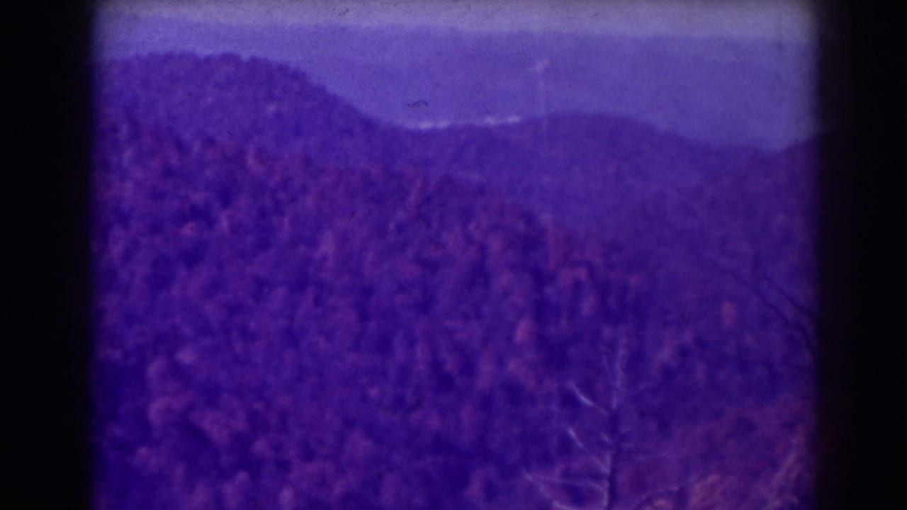 Distant mountain ridge and wooded slope with dark film borders.