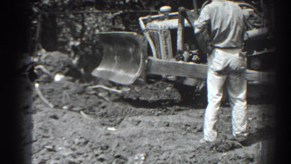 1938 Cumberland, Maryland frame showing a man standing beside the blade of a tracked front-loader at the muddy site.