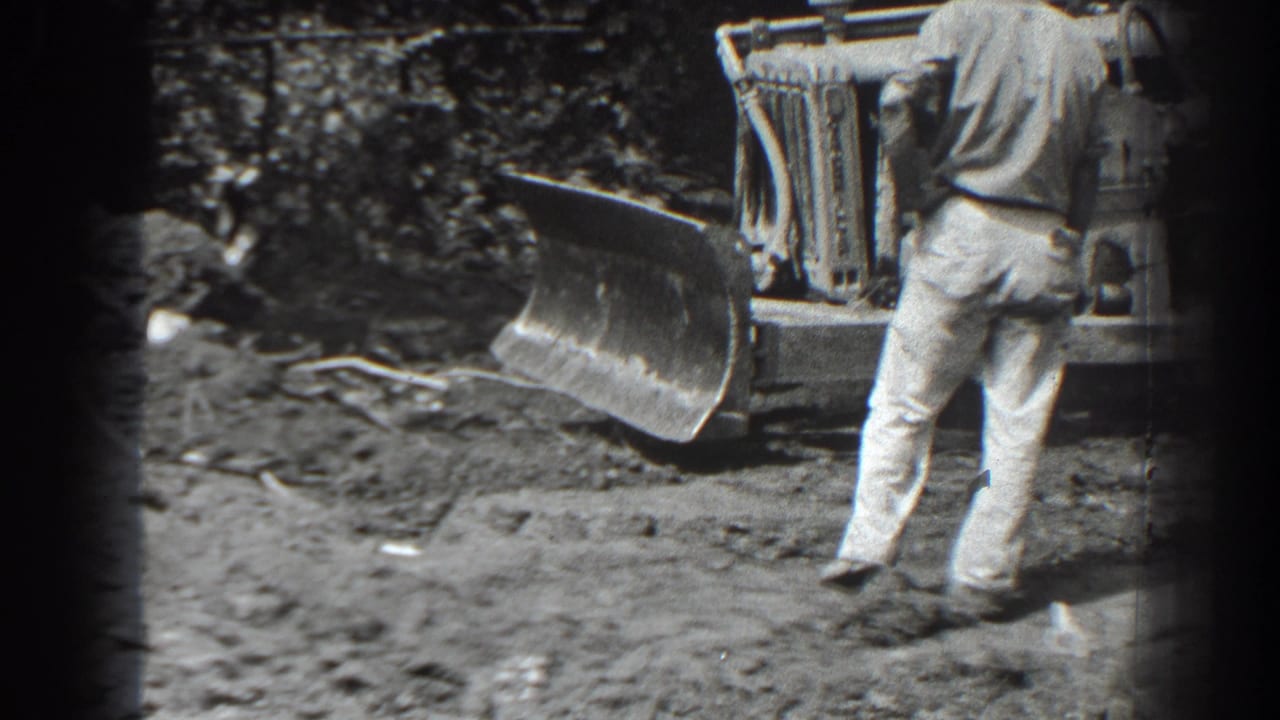 Man in light pants stands beside a tracked bulldozer at a muddy outdoor site.
