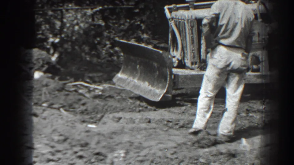 In 1938 Cumberland, Maryland footage, a man in light clothing stands near a bulldozer blade on churned ground.