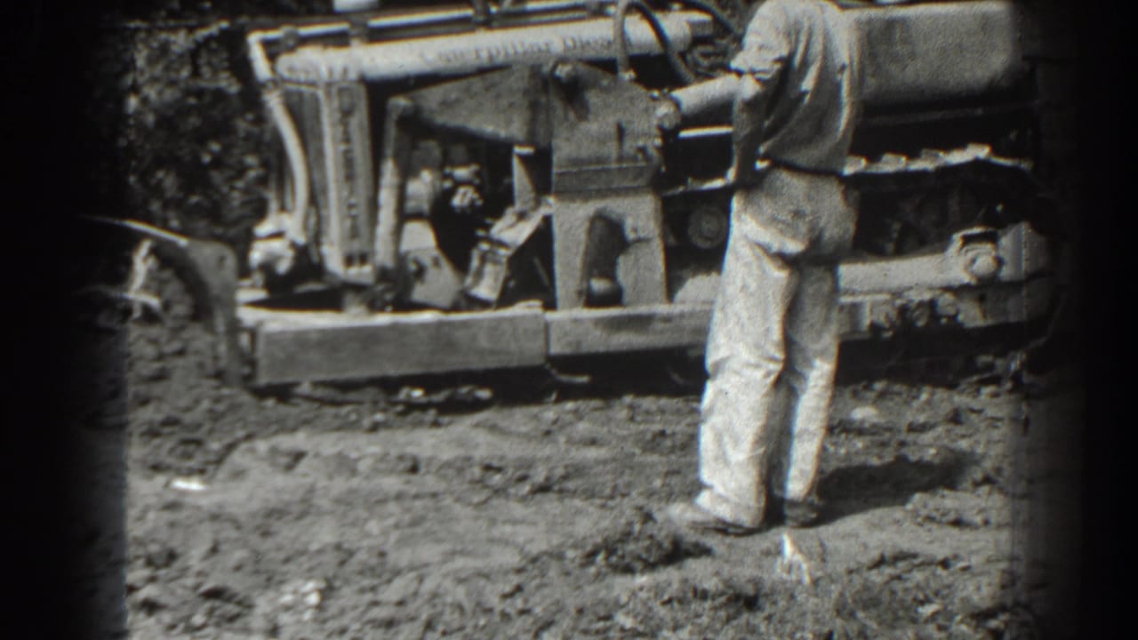 Man stands near the side of a bulldozer with tracks visible on rough ground.