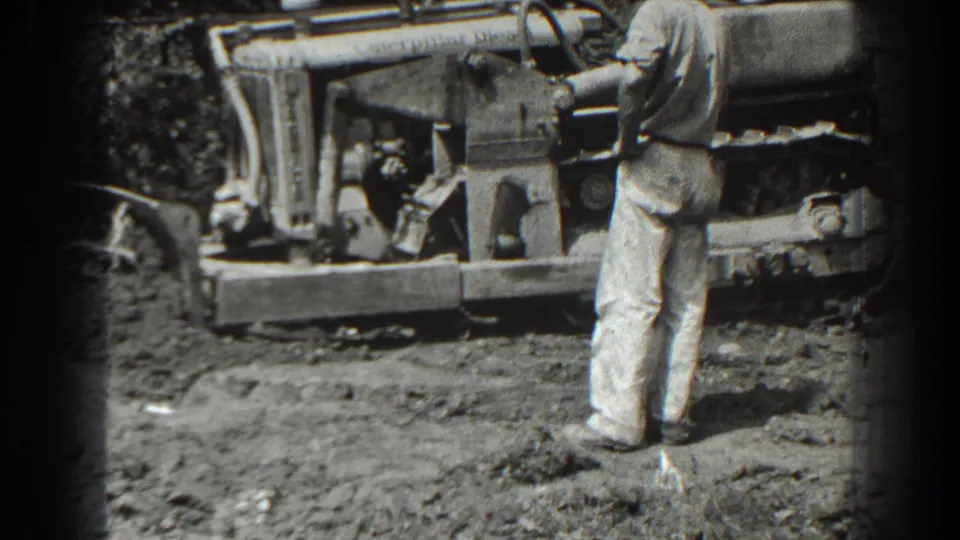 A man in light pants watches the side of a bulldozer in the 1938 Cumberland, Maryland construction footage.