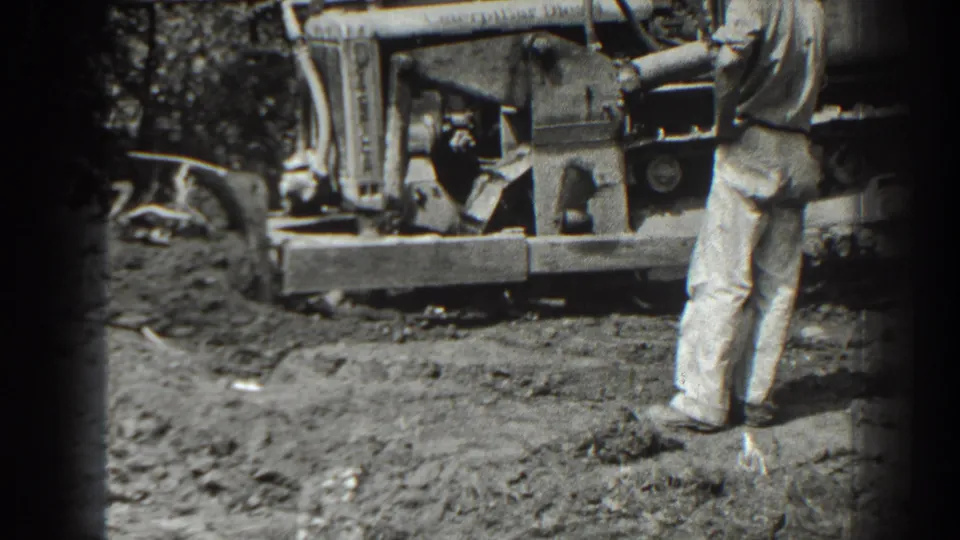 The bulldozer is framed closer as a man stands at the right edge of the 1938 Cumberland construction scene.