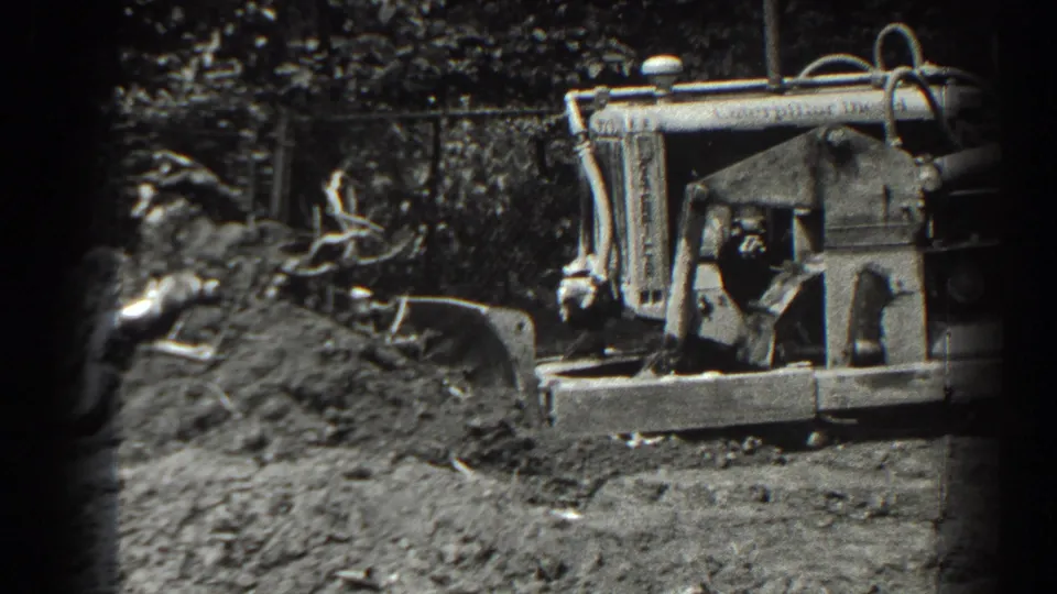 1938 Cumberland, Maryland 8mm frame showing a tracked tractor at a dirt mound with roots and rough ground nearby.