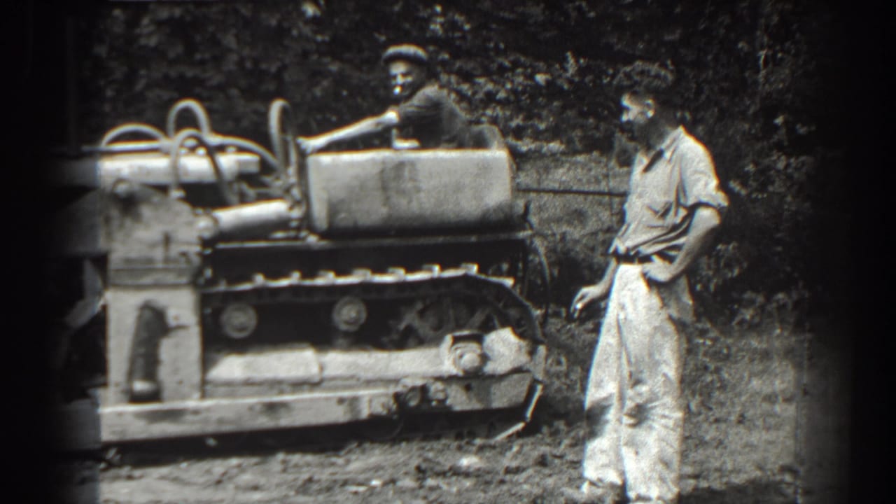 Tracked tractor beside a standing man in light clothing.