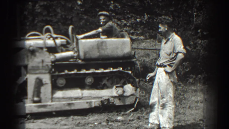 A man stands near the tracked tractor as the driver continues operating it in the Cumberland, Maryland home movie.