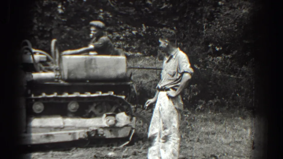 The onlooker in light trousers watches the tracked tractor at close range in the 1938 outdoor scene.