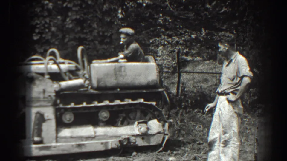 The driver and standing onlooker remain near the tracked tractor in this black-and-white 1938 Cumberland scene.