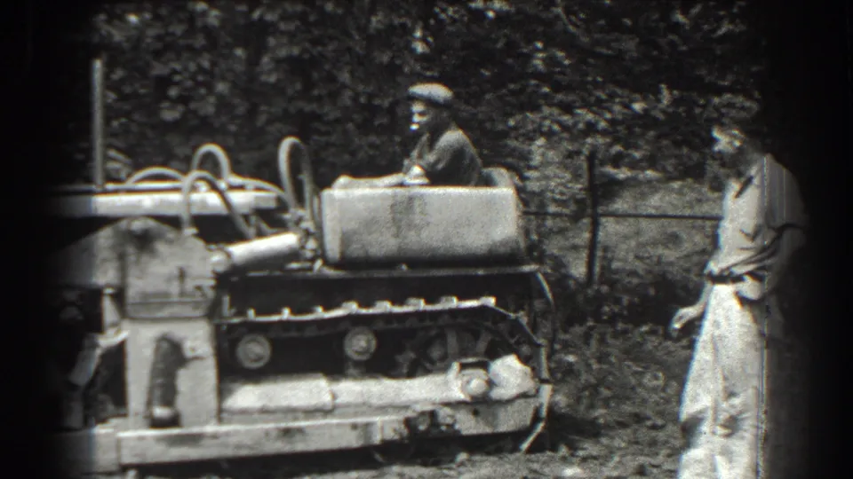 In Cumberland, Maryland, 1938, a man in a flat cap operates a tracked bulldozer while another man stands beside the rough ground.