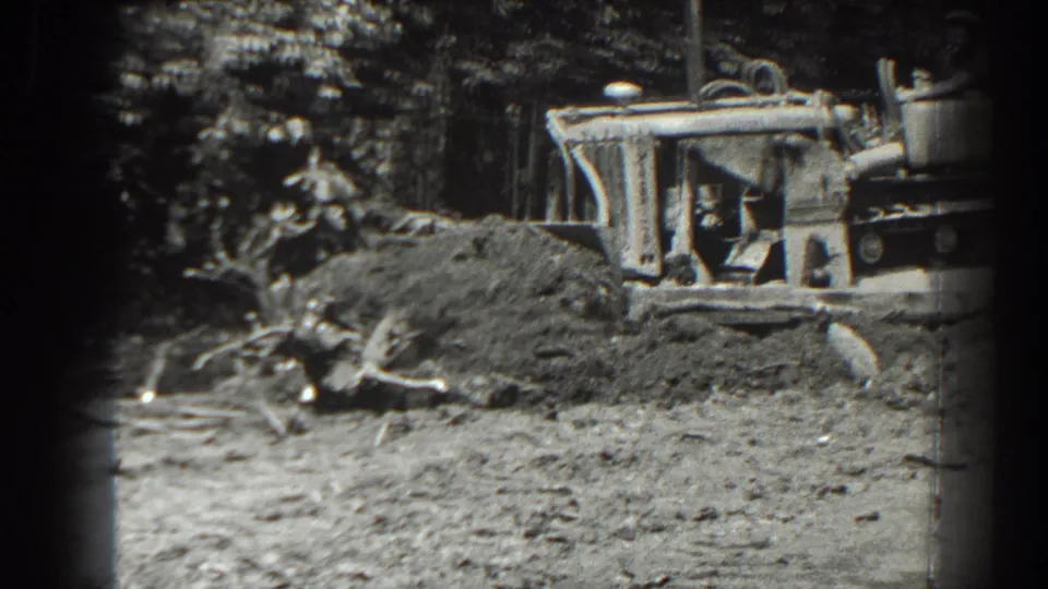 The 1938 Cumberland footage shows the bulldozer blade moving earth around stumps and roots in a rough outdoor work area.