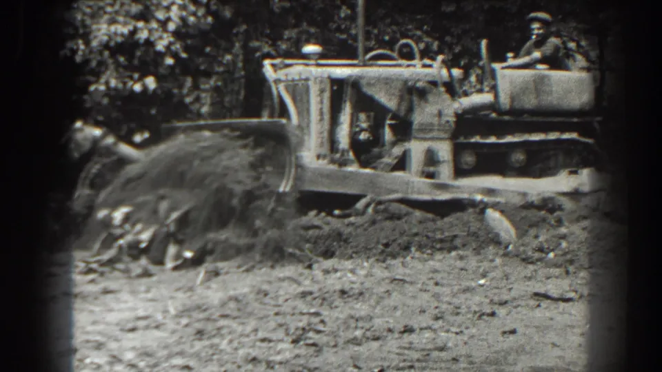 A side view shows the vintage tracked bulldozer working through churned soil, with the operator seated behind the blade mechanism.