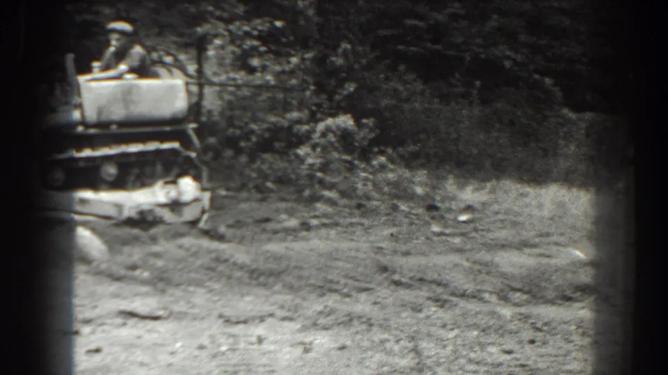 Late frame from the 1938 Cumberland clip showing the operator and tractor partly leaving view across a dirt clearing with trees behind.
