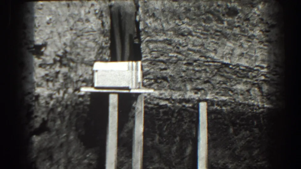 1938 Cumberland construction detail showing rough wall texture, a pale mounted form or bracket, and vertical supports in grainy 8mm footage.