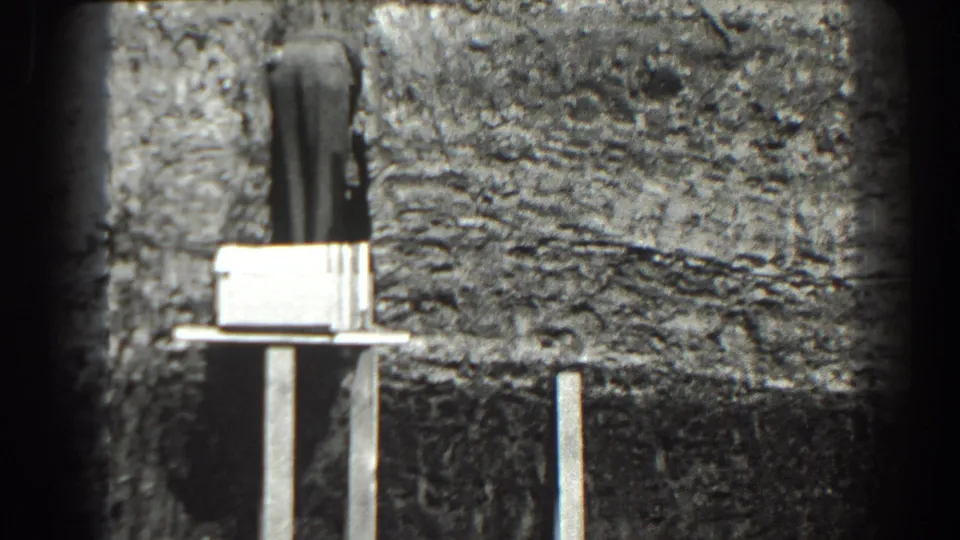 Grainy 8mm frame from Cumberland showing a rough construction surface, supported pale formwork, and shadowed excavation below.