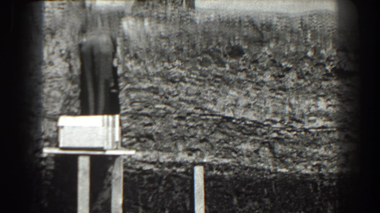 Man standing by a dug hillside with a pale box or board on a stand in front.