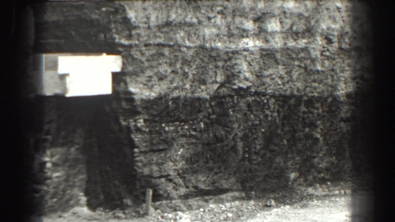 Rough stone tunnel wall with a bright rectangular light and debris on the floor.