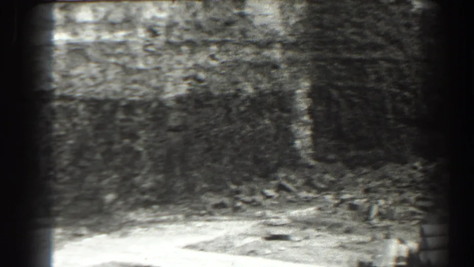 1938 Cumberland, Maryland 8mm frame showing a shadowed stone interior with scattered rubble and a soft bright strip along the floor.