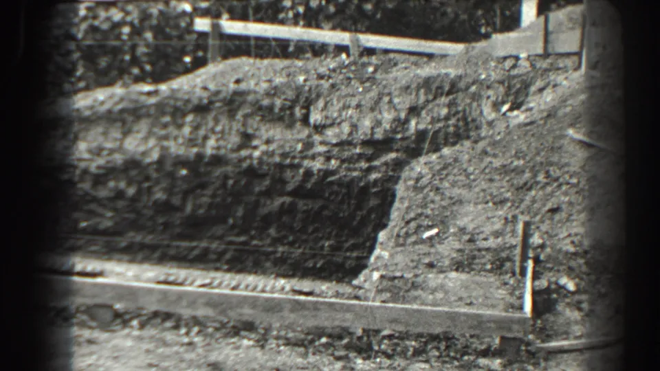1938 Cumberland, Maryland home-movie frame showing an exposed dirt cut, plank edging, scattered debris, and rough ground.