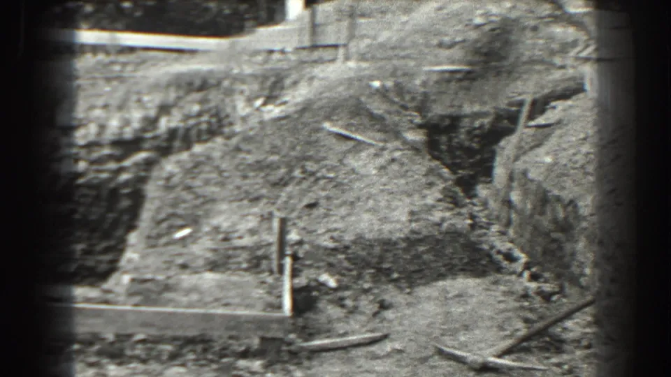 1938 Cumberland, Maryland frame showing a rough excavation area with a trench, scattered boards, exposed soil, and a small hand tool.