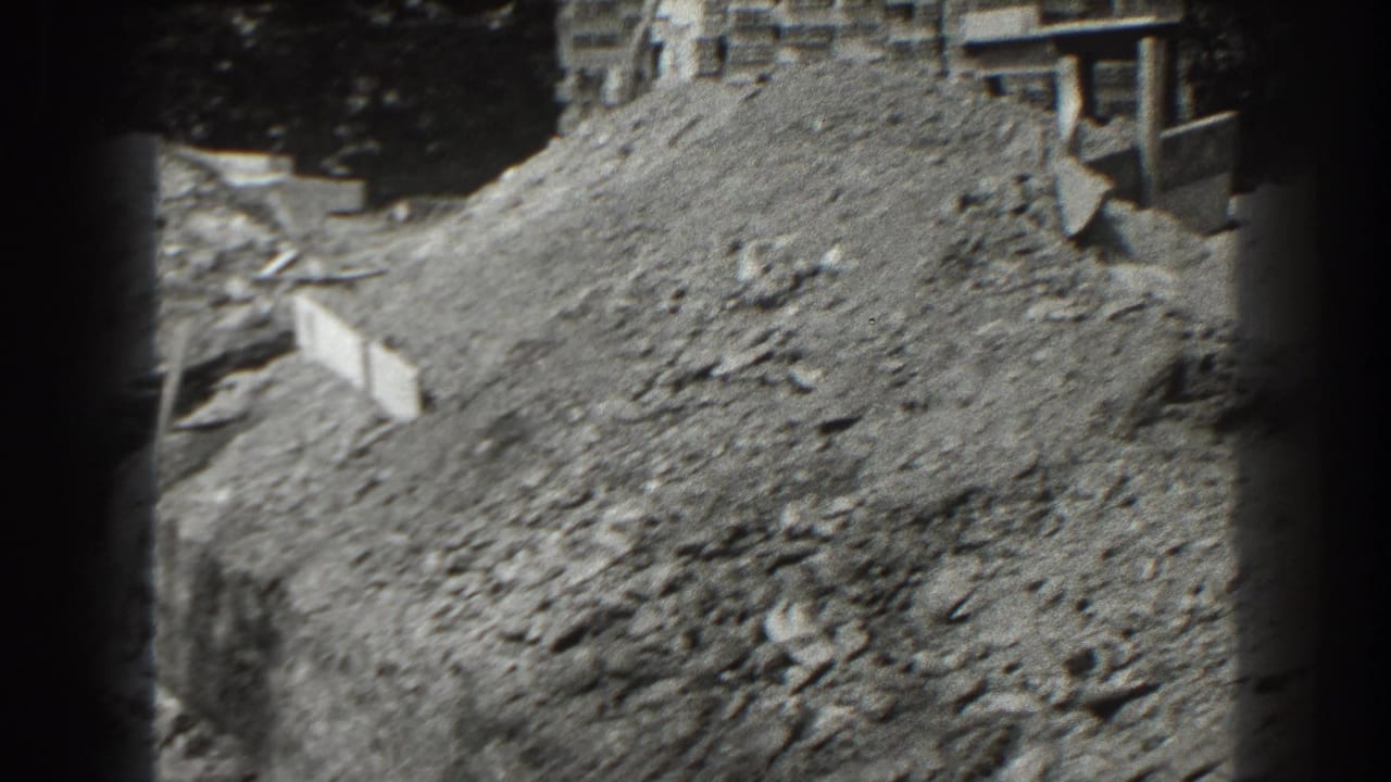Large dirt pile and rough ground beside stacked blocks and a building.