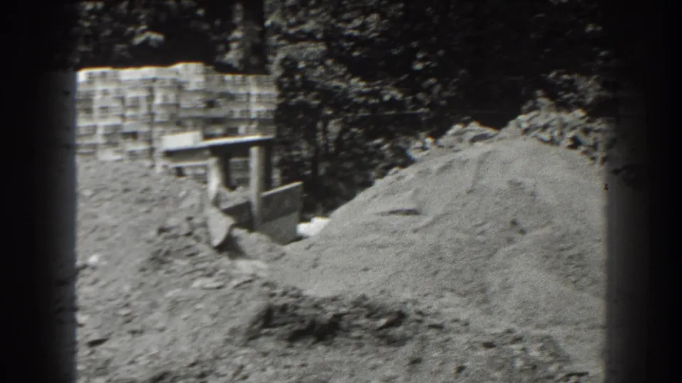 1938 Cumberland footage appears to show a small bulldozer or loader beside a dirt pile, with concrete blocks and trees behind it.
