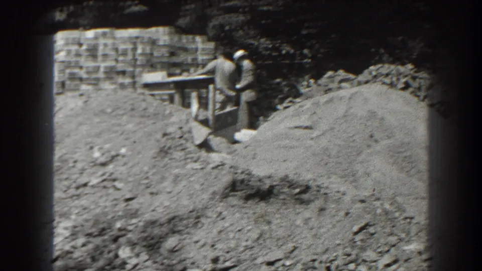 Two men in period clothing stand near a wooden structure at a Cumberland, Maryland construction site in the supplied 1938 footage.