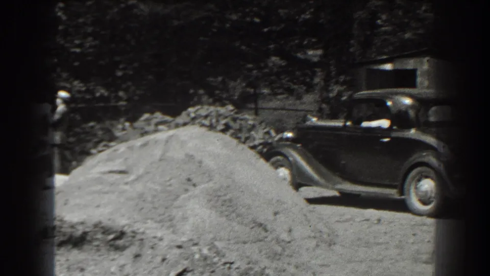 1938 Cumberland, Maryland home-movie frame showing a dark sedan parked beside a sand pile and trees.