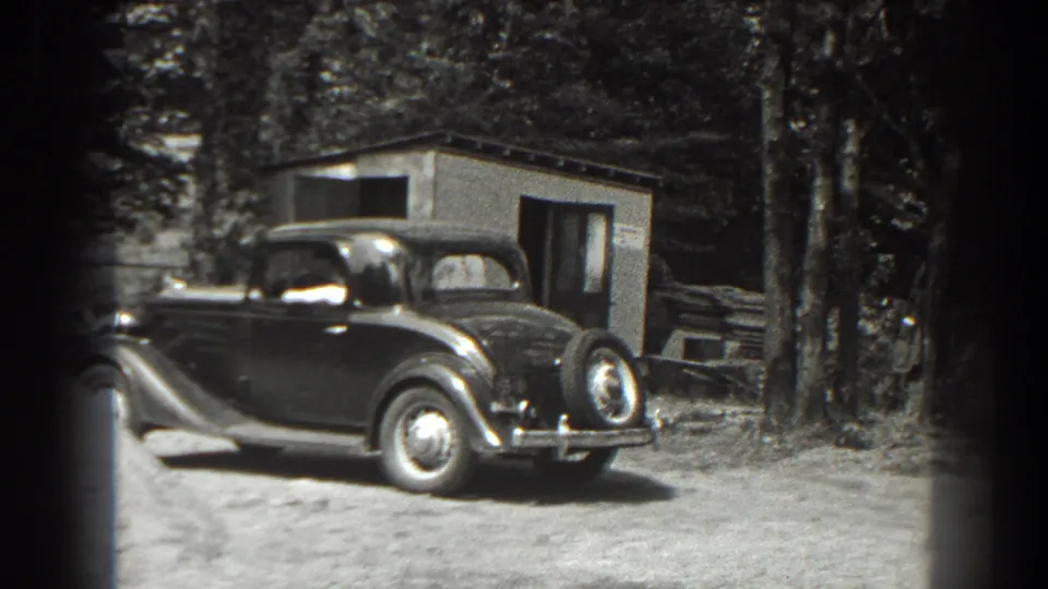 1938 Cumberland, Maryland home-movie frame showing the sedan, shed, trees, and partially visible adults near the work area.