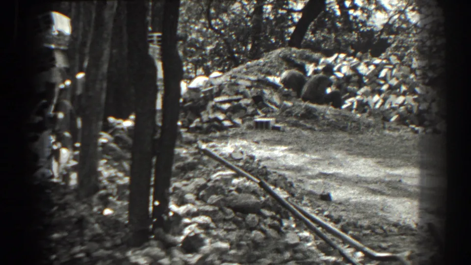 1938 Cumberland, Maryland frame showing work materials, trees, rocks, and a narrow rail or pipe in a wooded outdoor setting.