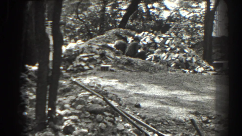 1938 Cumberland, Maryland home-movie frame showing a wooded work area with a trench, dirt path, rocks, and mounded earth.