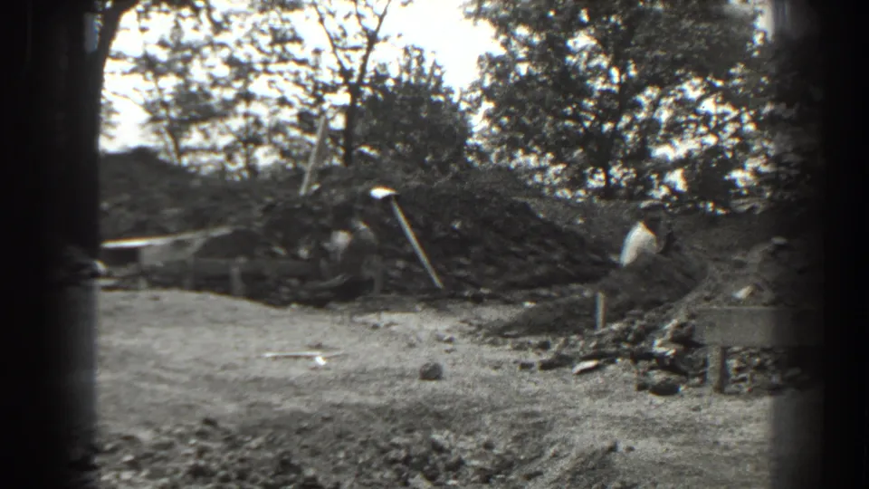 1938 Cumberland, Maryland frame with workers and shovels beside a trench, surrounded by dirt piles, rocks, and trees.