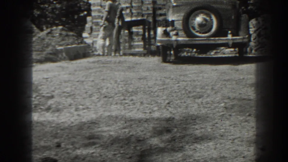 In the Cumberland work area, a man stands near stacked materials while a classic automobile is parked at the edge of the frame.