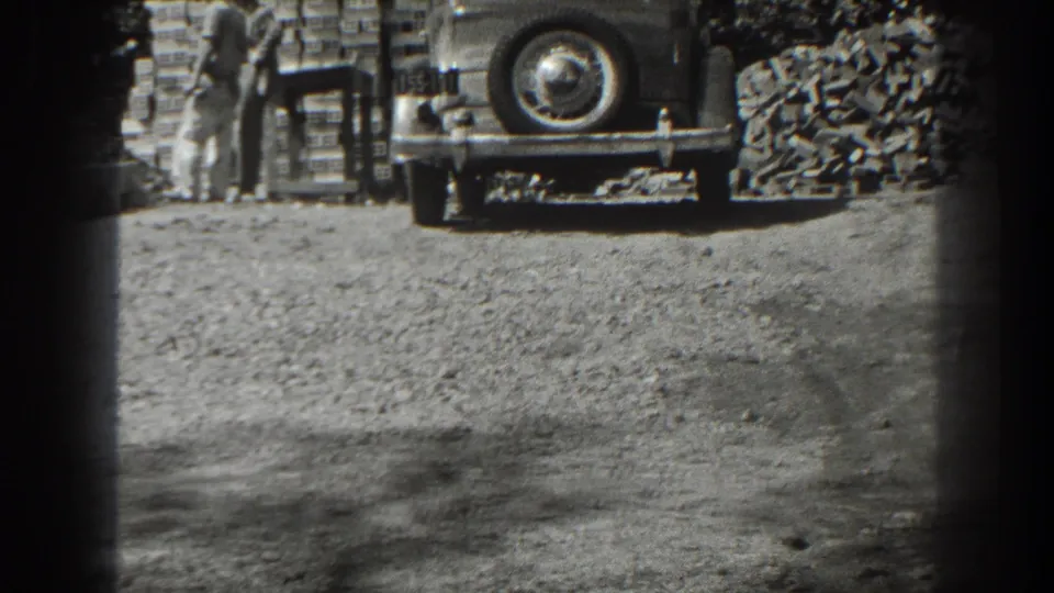 In Cumberland, Maryland in 1938, two men appear beside stacked bricks and a parked 1930s car on an unpaved roadside.
