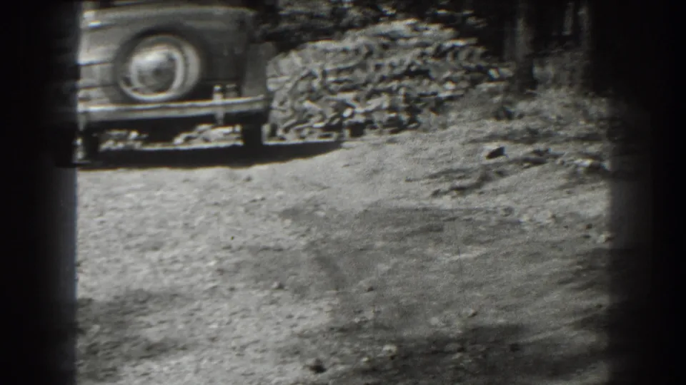 A parked 1930s automobile with a rear spare tire appears beside a large brick stack in the Cumberland, Maryland footage.
